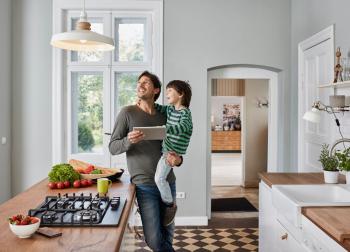 Man carrying child in arm, while looking at hanging light in kitchen