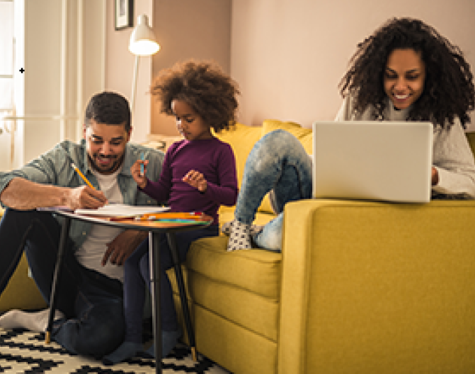 A lamp with an LED bulb lights up a living room where a family of three is sitting on a yellow couch.