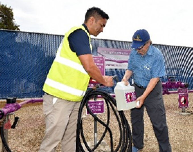 LADWP staff member assists customer with filling up a labeled recycled water jug at a refill station. 