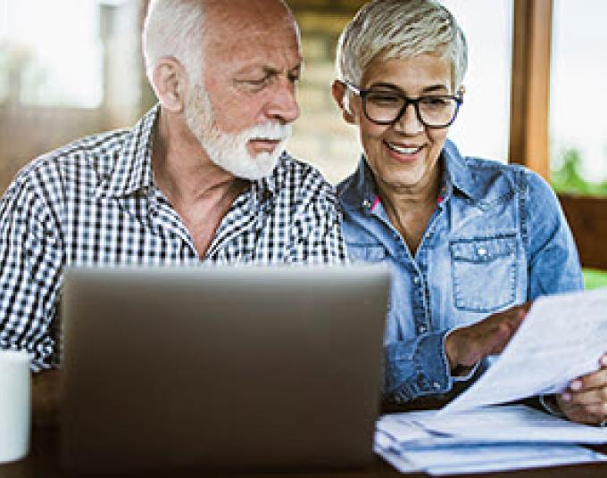 Two people sitting together looking at a piece of paper with a laptop on the table.