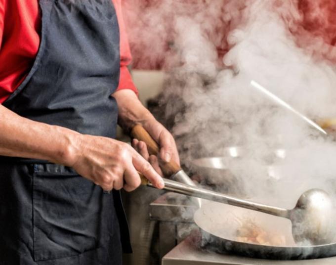 Person cooking over high heat with steam and smoke coming out of pan