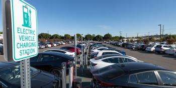 A sign says “Electric Vehicle Charging Station” next to rows of charging electric cars.