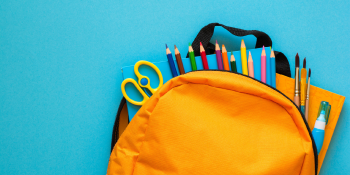 An orange backpack filled with school supplies like colored pencils and scissors on a blue background.