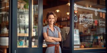 Smiling women with arms crossed leaning against door frame of store.