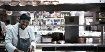 chef in kitchen with hanging pot lids above