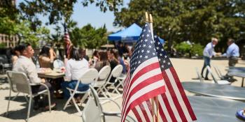 American flags with a background of people gathering in a park setting